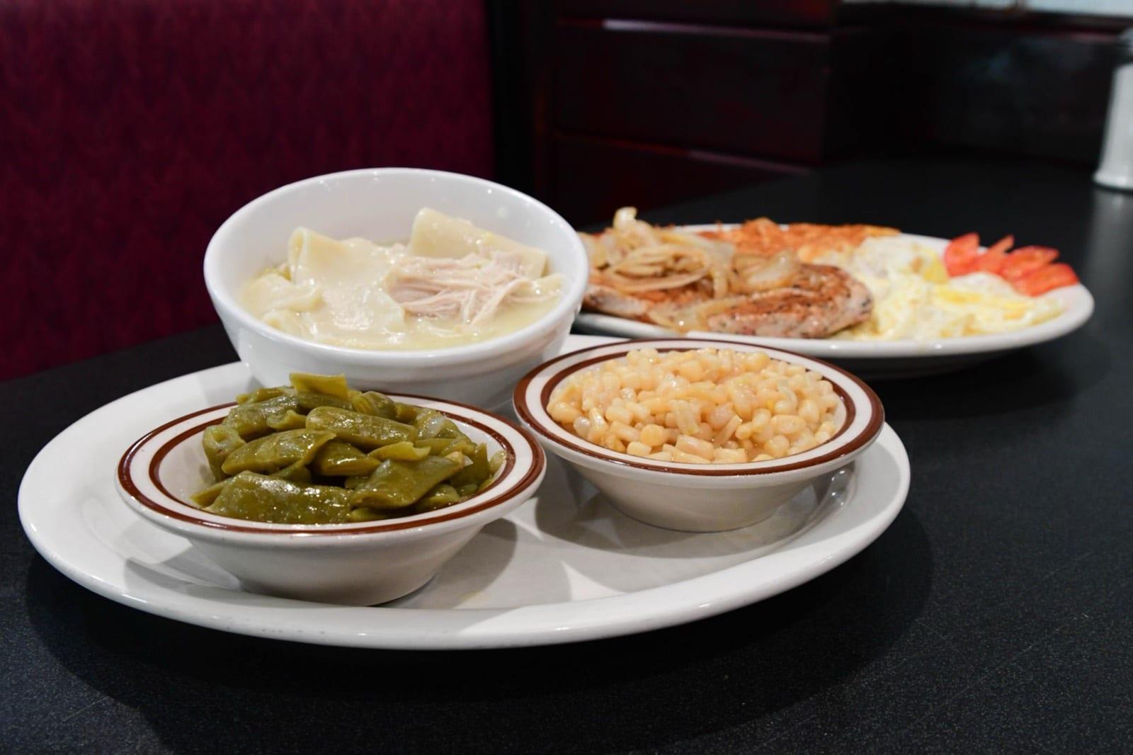 Chicken and dumplings with green beans and macaroni and cheese, with a pork chop and eggs plate behind, in the dining room at Ranch House Makarios in Vestavia Hills, AL