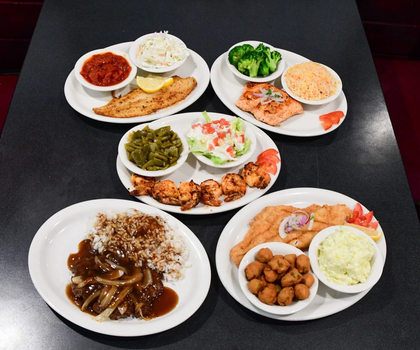 Spread of Southern and seafood plates including blackened fish, grilled salmon, shrimp skewers, hamburger steak over rice, and a fried fish platter at Ranch House Makarios in Vestavia Hills, AL